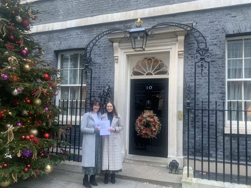 Chelcie and Becky are stood outside number 10 Downing street, holding copy of their report